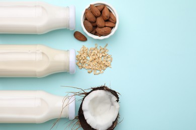 Photo of Different types of vegan milk in bottles and ingredients on light blue table, flat lay. Space for text