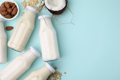 Different types of vegan milk in bottles and ingredients on light blue table, flat lay. Space for text