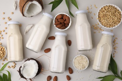 Photo of Different types of vegan milk in bottles with ingredients and leaves on light grey table, flat lay