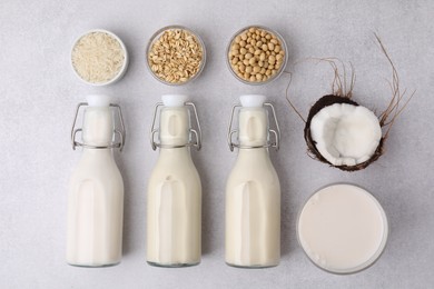 Different types of vegan milk in bottles and ingredients on light grey table, flat lay