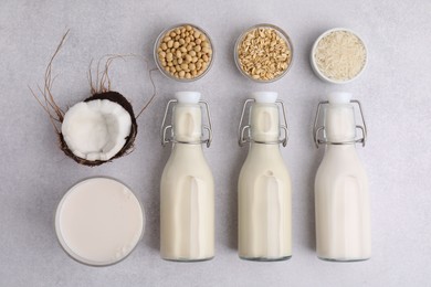 Different types of vegan milk in bottles and ingredients on light grey table, flat lay