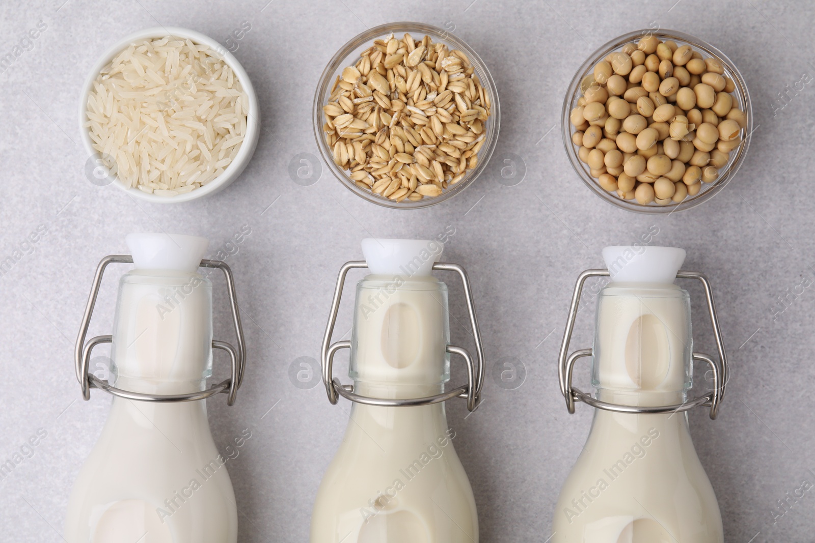 Photo of Different types of vegan milk in bottles and ingredients on light grey table, flat lay