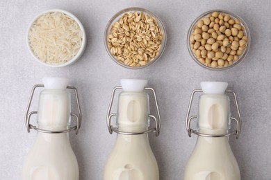 Different types of vegan milk in bottles and ingredients on light grey table, flat lay