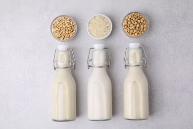 Different types of vegan milk in bottles and ingredients on light grey table, flat lay