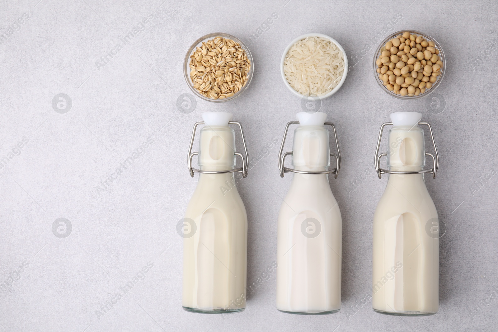 Photo of Different types of vegan milk in bottles and ingredients on light grey table, flat lay. Space for text