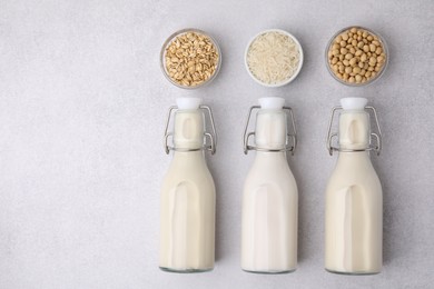 Different types of vegan milk in bottles and ingredients on light grey table, flat lay. Space for text