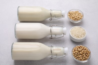 Photo of Different types of vegan milk in bottles and ingredients on light grey table