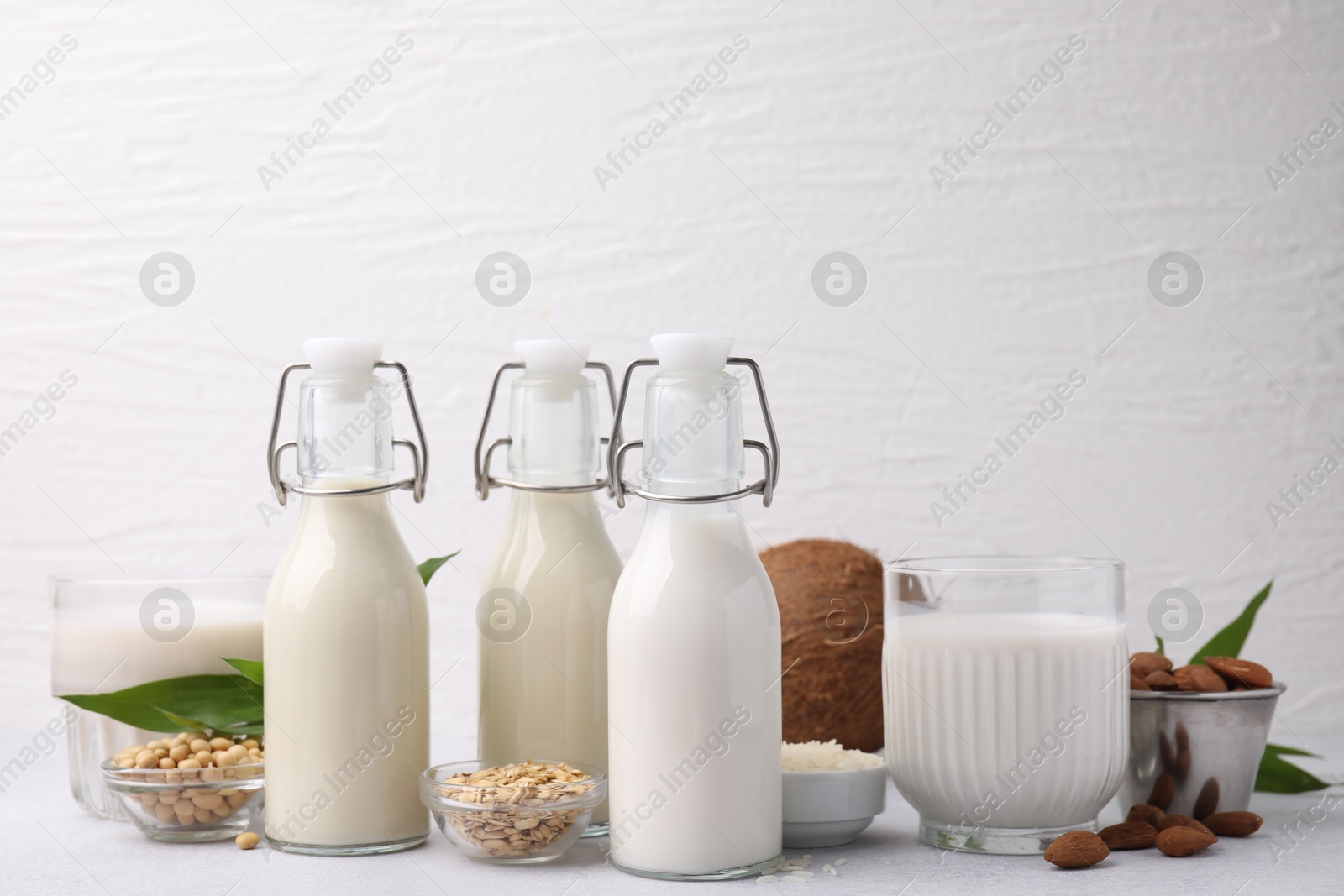 Photo of Different types of vegan milk and ingredients on light grey table