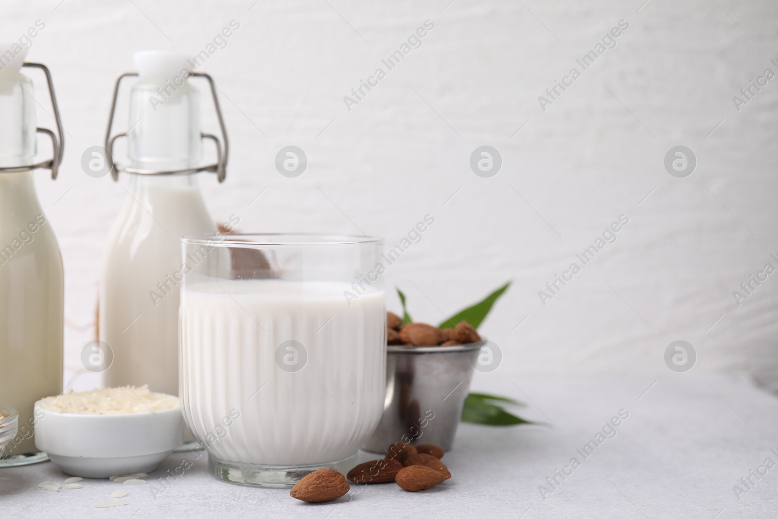 Photo of Different types of vegan milk and ingredients on light grey table, space for text