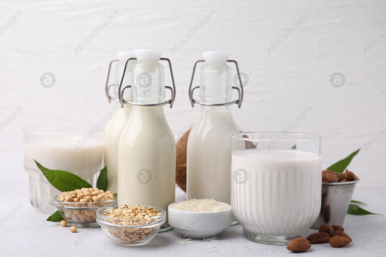 Photo of Different types of vegan milk and ingredients on light grey table