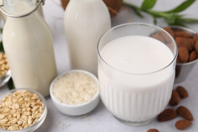 Different types of vegan milk and ingredients on light grey table, closeup