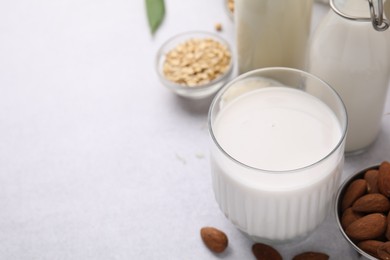 Different types of vegan milk and ingredients on light grey table, space for text