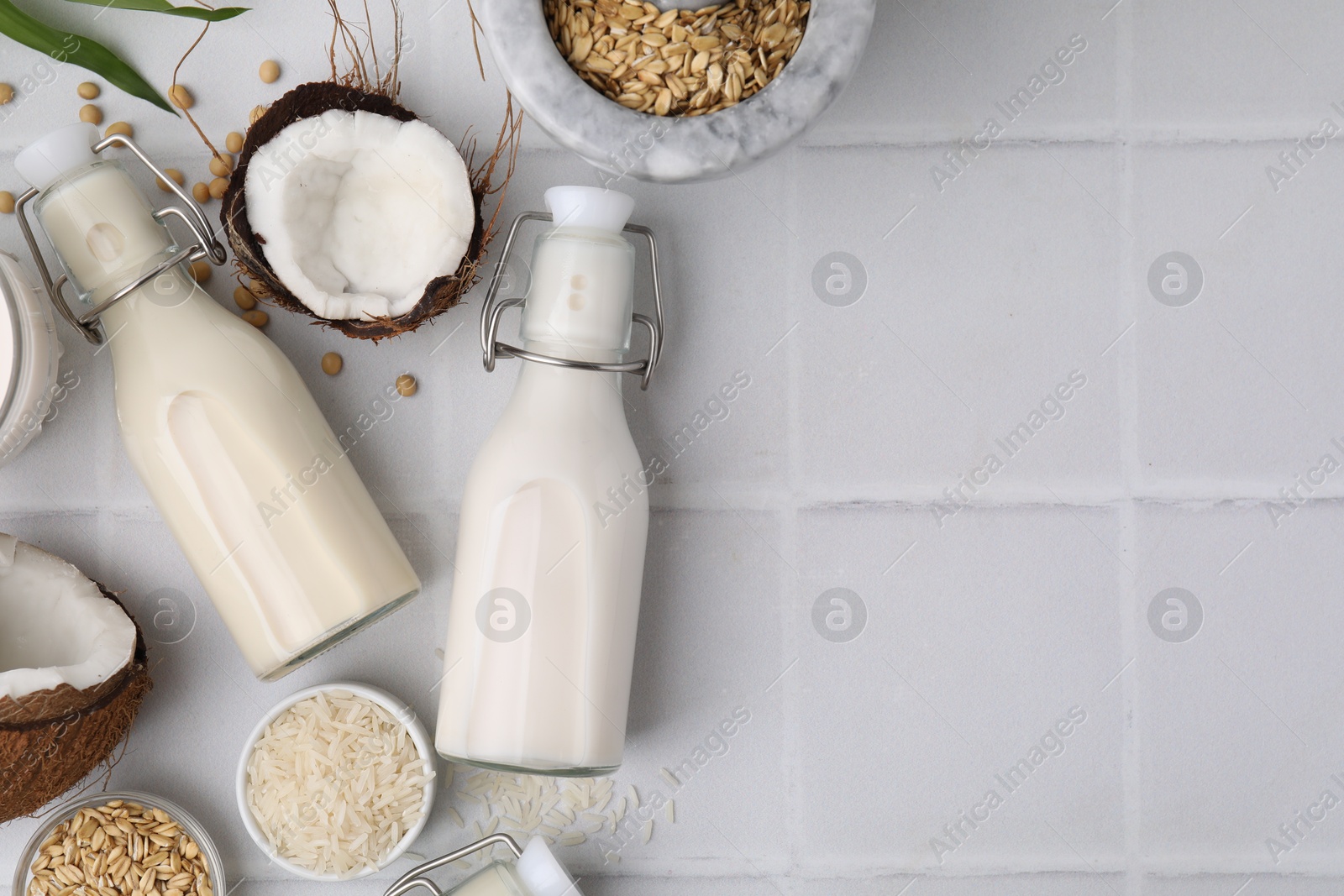 Photo of Different types of vegan milk in bottles and ingredients on white tiled table, flat lay. Space for text