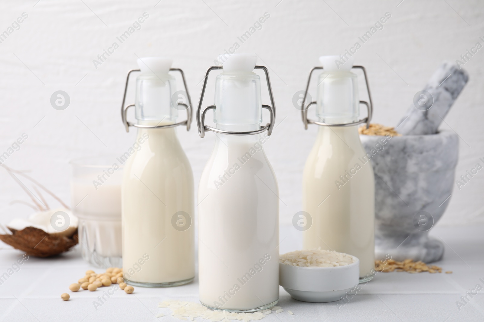 Photo of Different types of vegan milk and ingredients on white tiled table