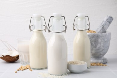 Different types of vegan milk and ingredients on white tiled table