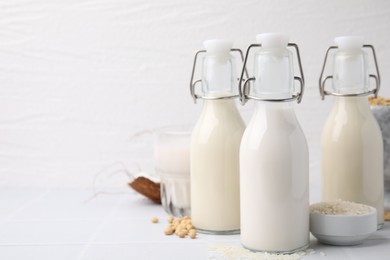 Photo of Different types of vegan milk and ingredients on white tiled table, space for text