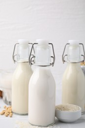 Different types of vegan milk in bottles and ingredients on white table, closeup