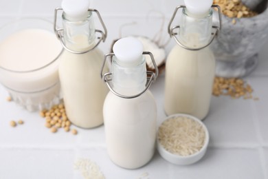 Photo of Different types of vegan milk and ingredients on white tiled table, closeup