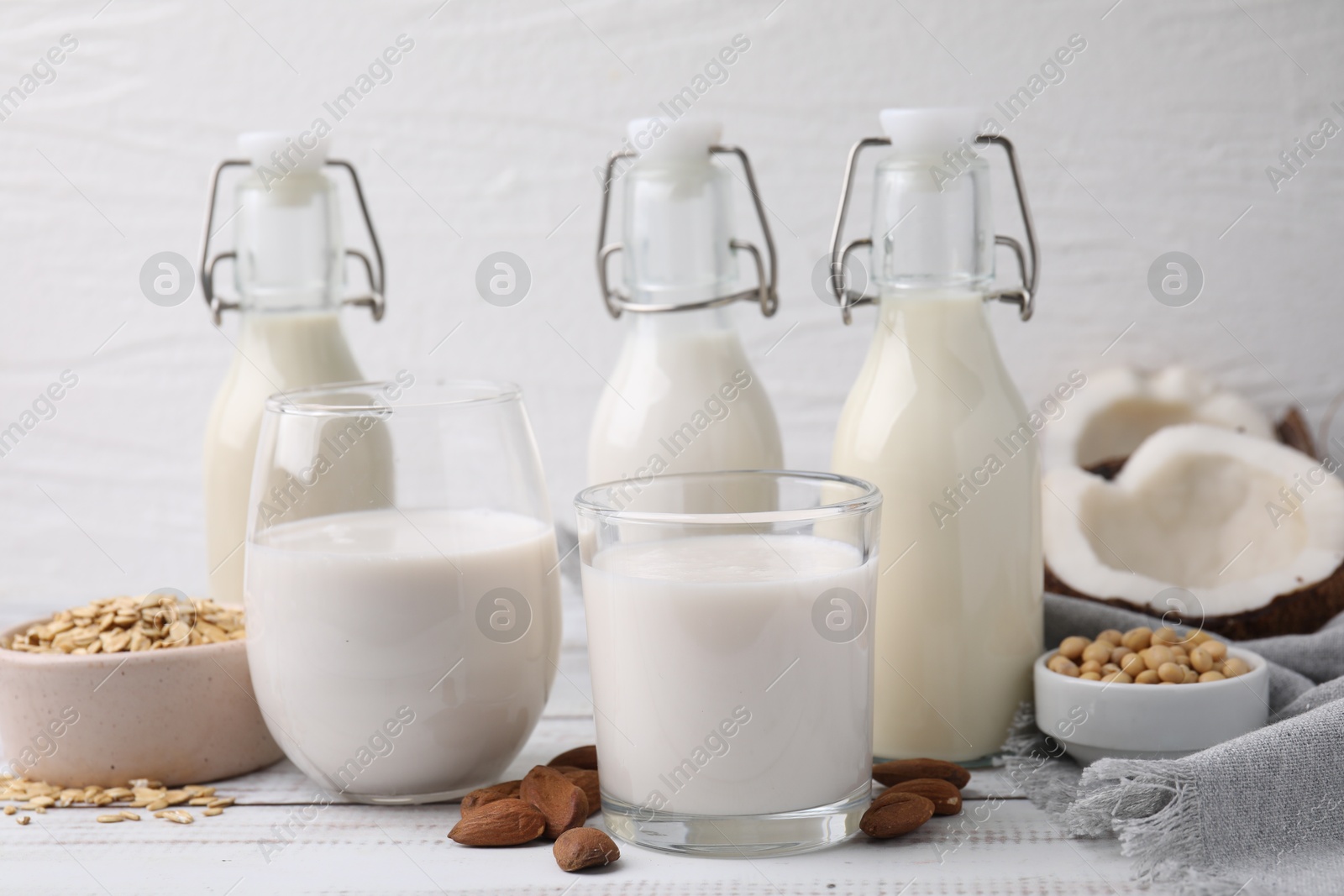 Photo of Different types of vegan milk and ingredients on white wooden table