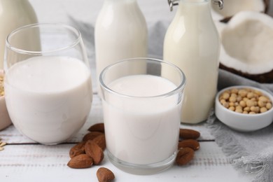 Photo of Different types of vegan milk and ingredients on white wooden table, closeup