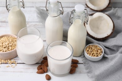 Different types of vegan milk and ingredients on white wooden table