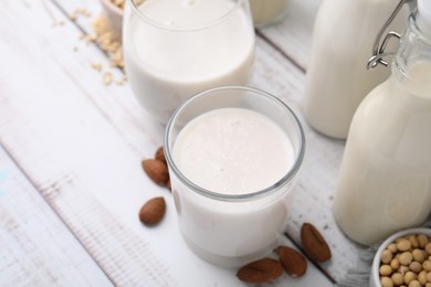 Photo of Different types of vegan milk and ingredients on white wooden table, closeup