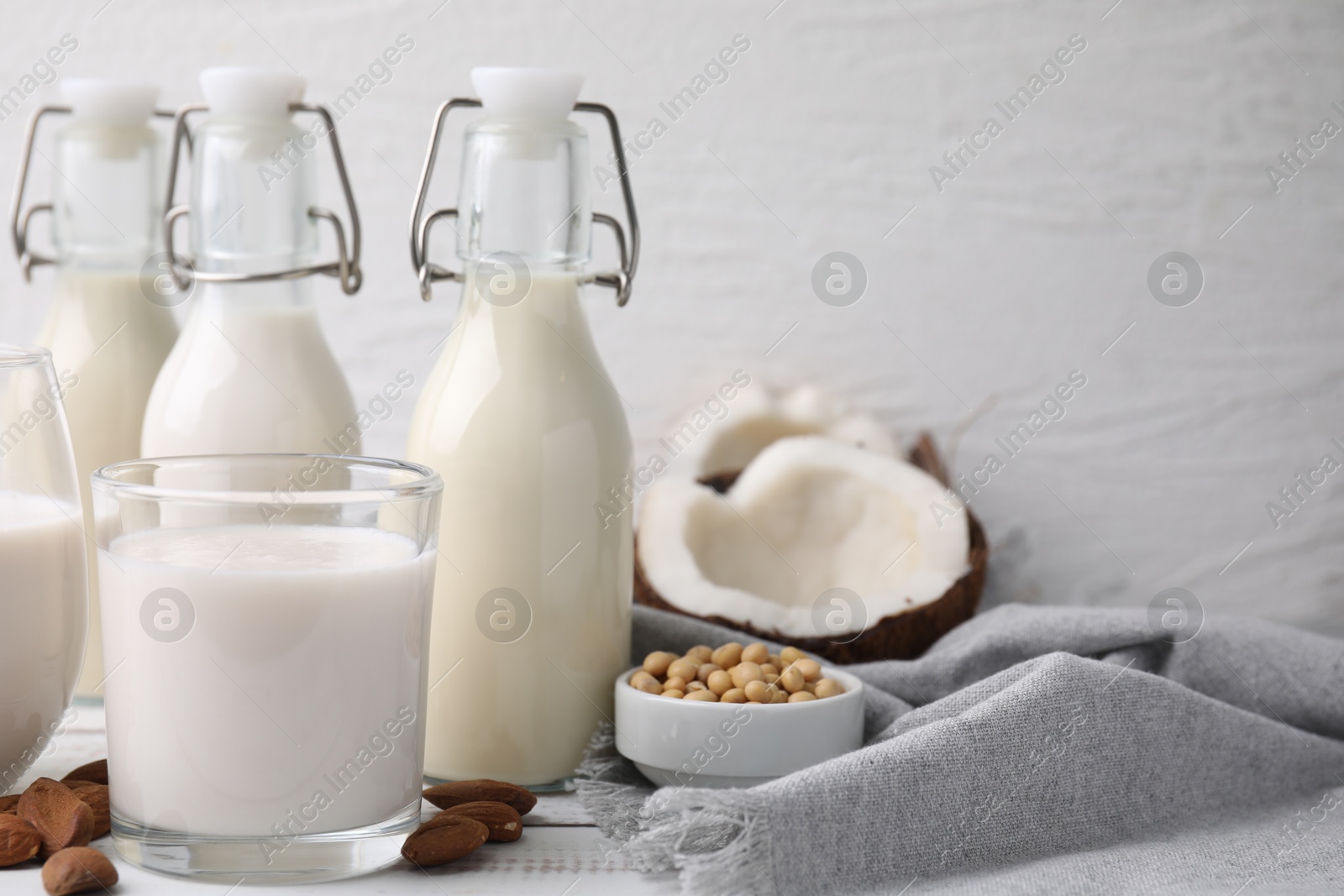 Photo of Different types of vegan milk and ingredients on white wooden table