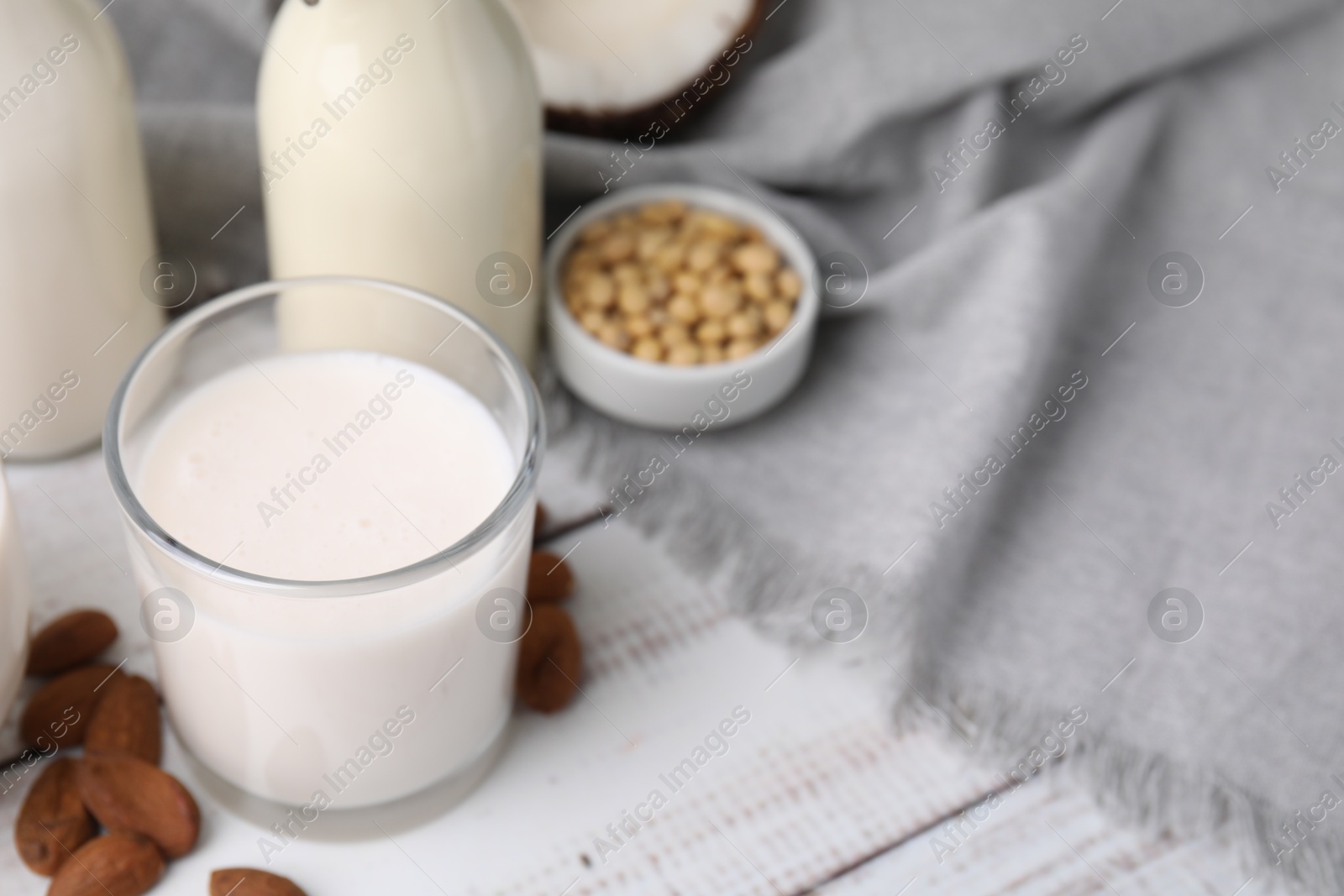 Photo of Different types of vegan milk and ingredients on white wooden table, closeup. Space for text