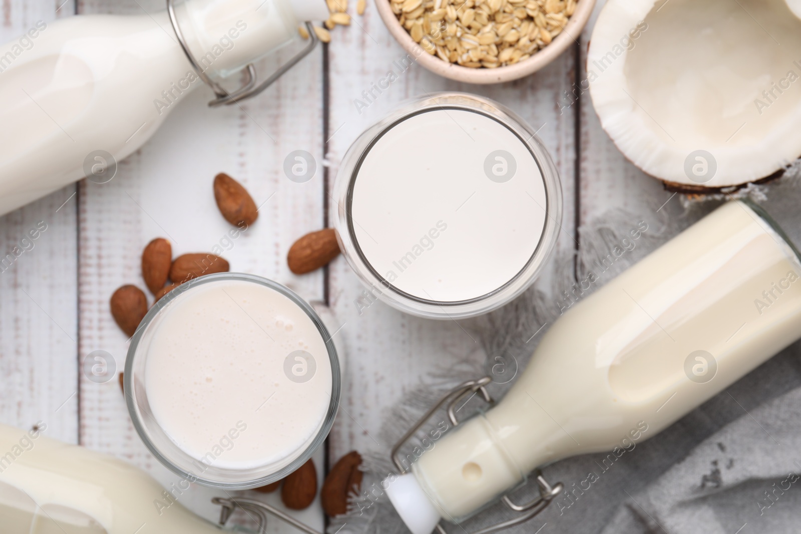 Photo of Different types of vegan milk and ingredients on white wooden table, flat lay