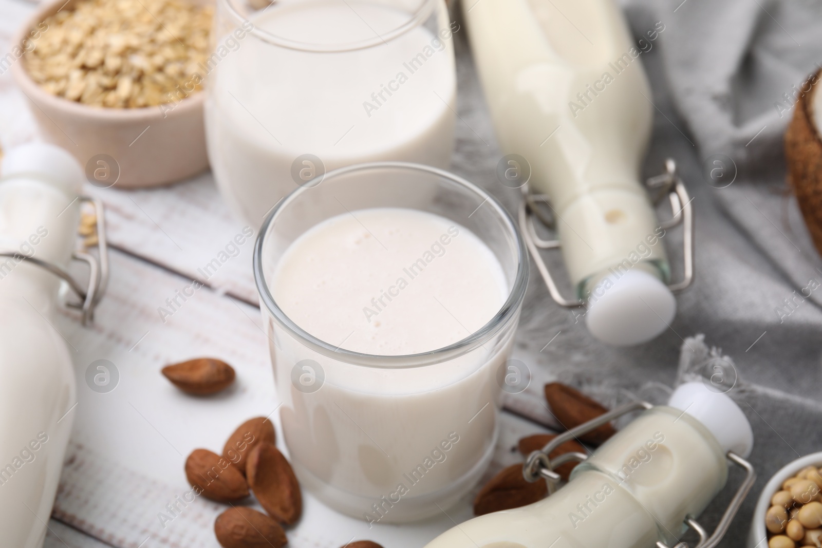 Photo of Different types of vegan milk and ingredients on white wooden table, closeup