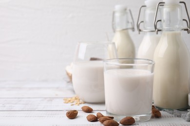 Different types of vegan milk and ingredients on white wooden table. Space for text