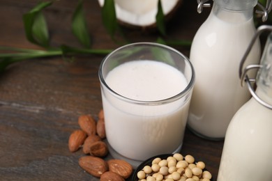 Photo of Different types of vegan milk and ingredients on wooden table, closeup