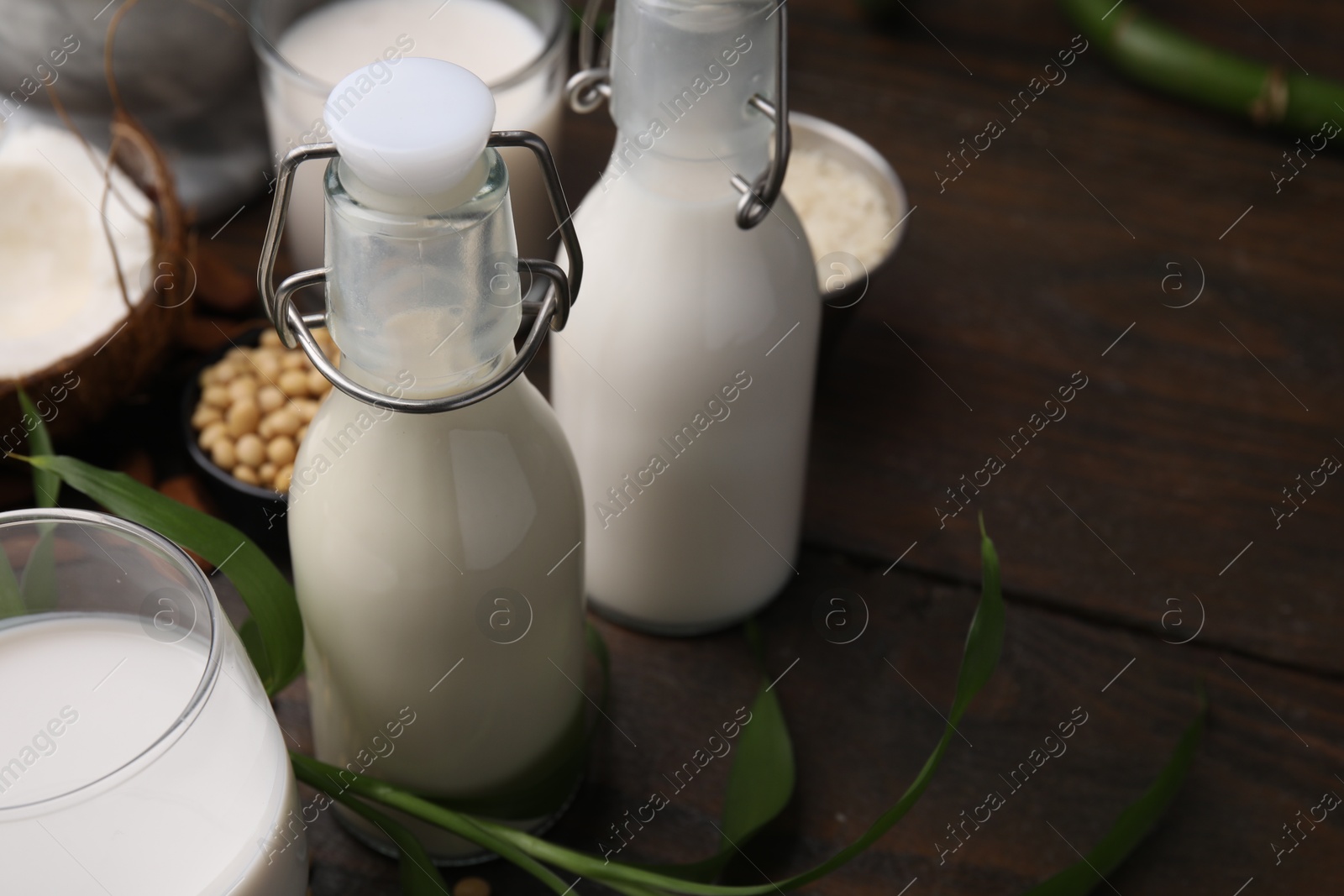 Photo of Different types of vegan milk and ingredients on wooden table, closeup