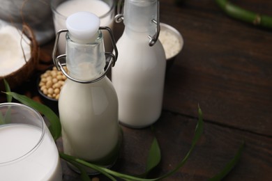 Photo of Different types of vegan milk and ingredients on wooden table, closeup