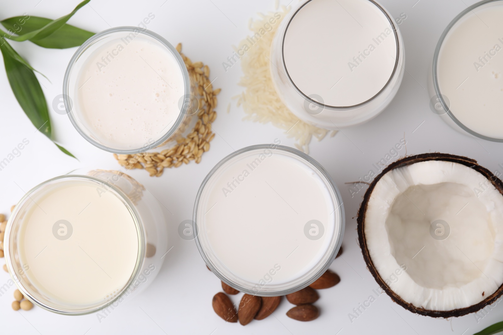 Photo of Different types of vegan milk and ingredients on white table, flat lay