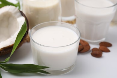 Photo of Different types of vegan milk and ingredients on white table, closeup