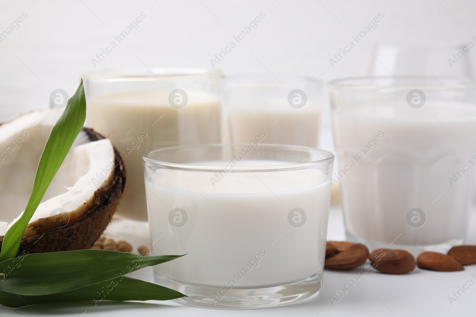 Photo of Different types of vegan milk and ingredients on white table, closeup