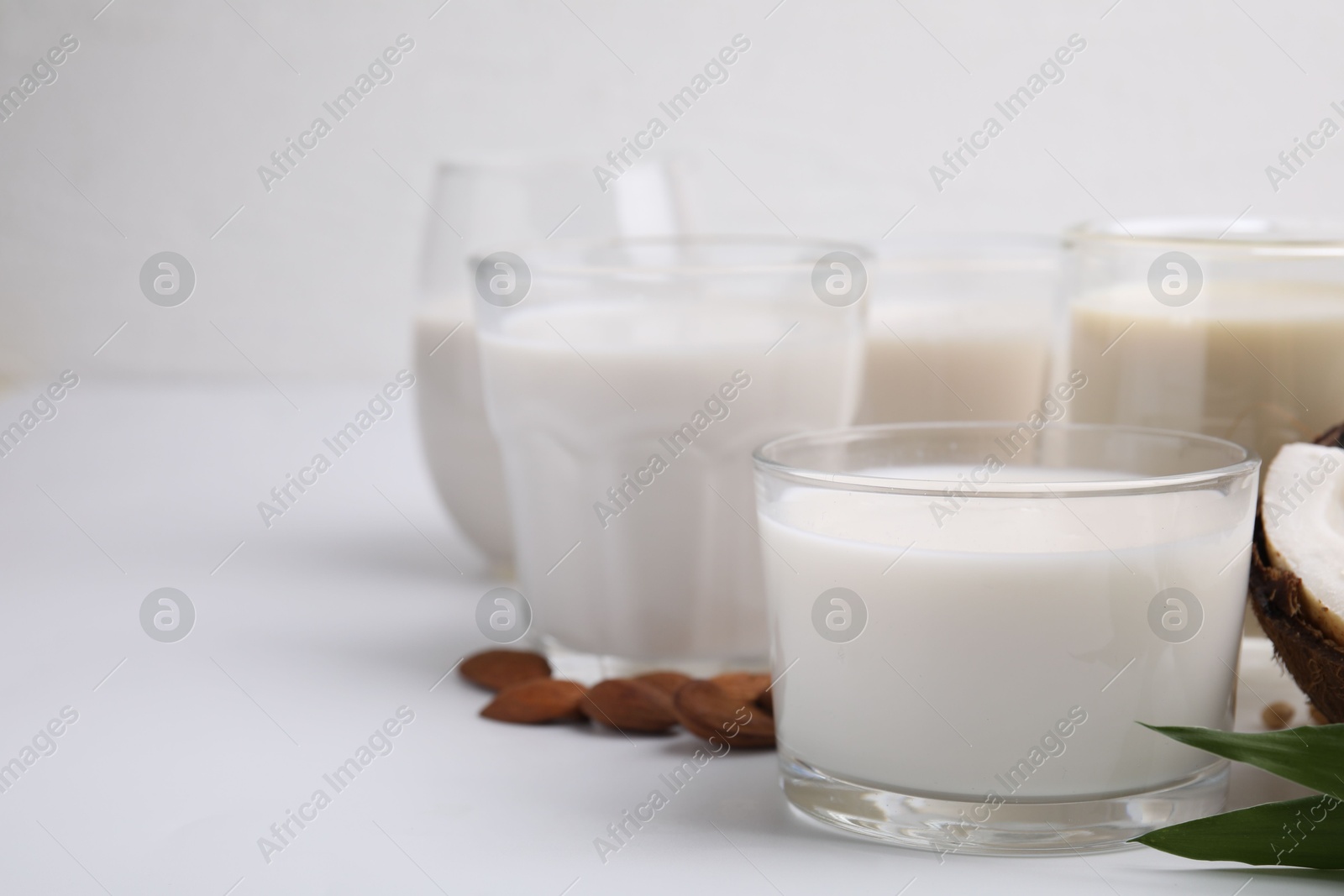 Photo of Different types of vegan milk and ingredients on white table, closeup