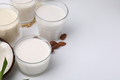 Photo of Different types of vegan milk and ingredients on white table, closeup. Space for text