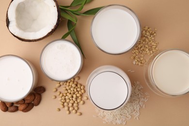 Photo of Different types of vegan milk and ingredients on beige table, flat lay