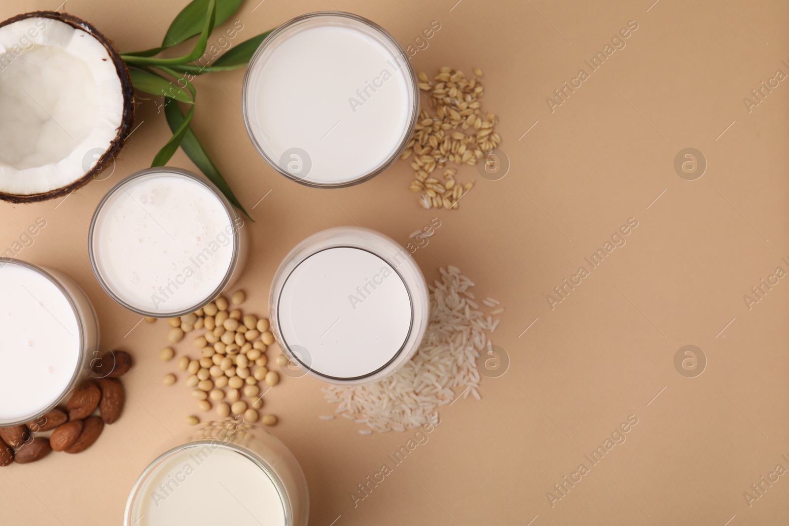 Photo of Different types of vegan milk and ingredients on beige table, flat lay. Space for text