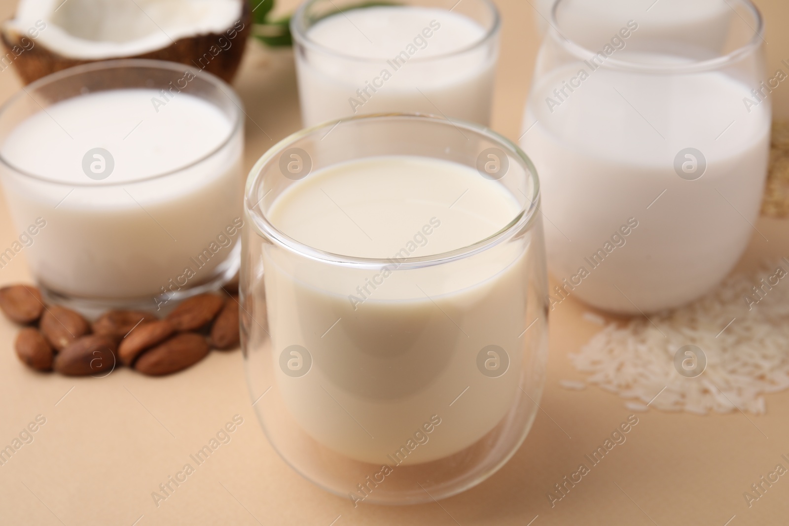 Photo of Different types of vegan milk and ingredients on beige table, closeup