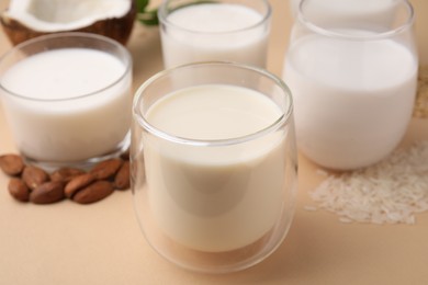 Different types of vegan milk and ingredients on beige table, closeup