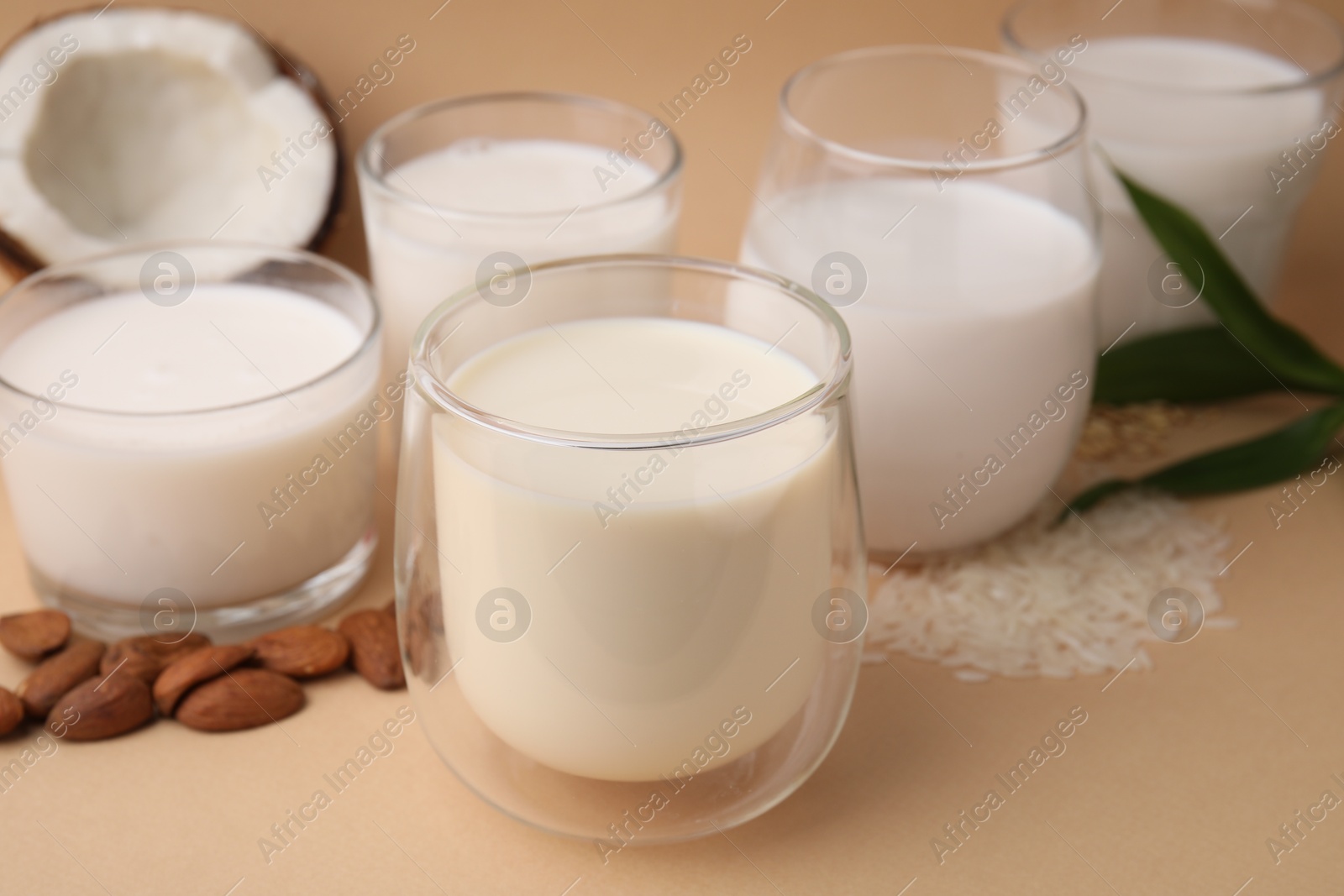 Photo of Different types of vegan milk and ingredients on beige table, closeup