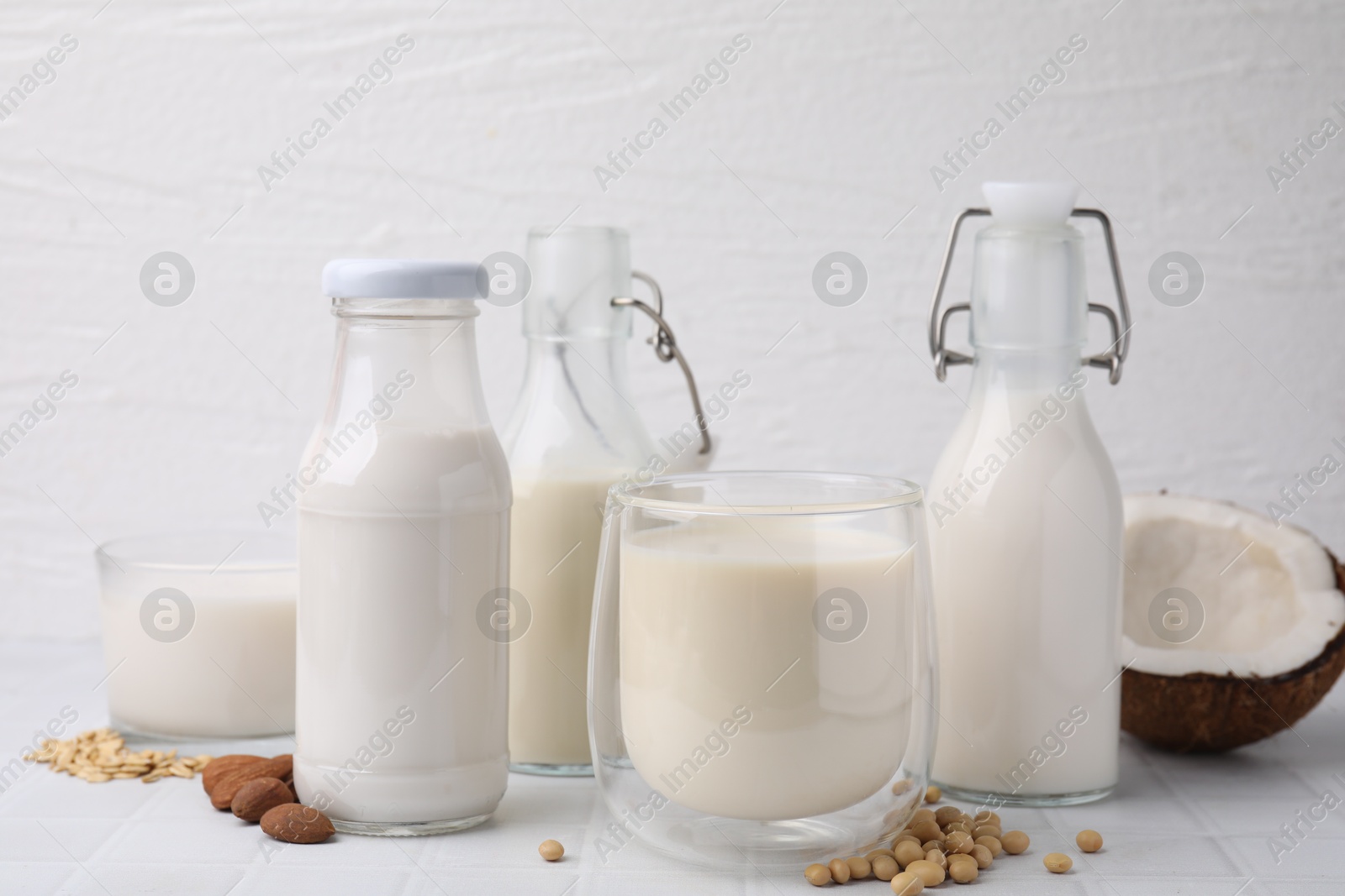 Photo of Different types of vegan milk and ingredients on white tiled table