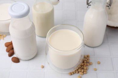 Photo of Different types of vegan milk and ingredients on white tiled table, closeup