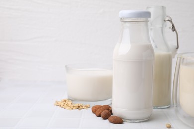 Different types of vegan milk and ingredients on white tiled table. Space for text