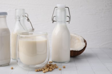 Different types of vegan milk and ingredients on white tiled table