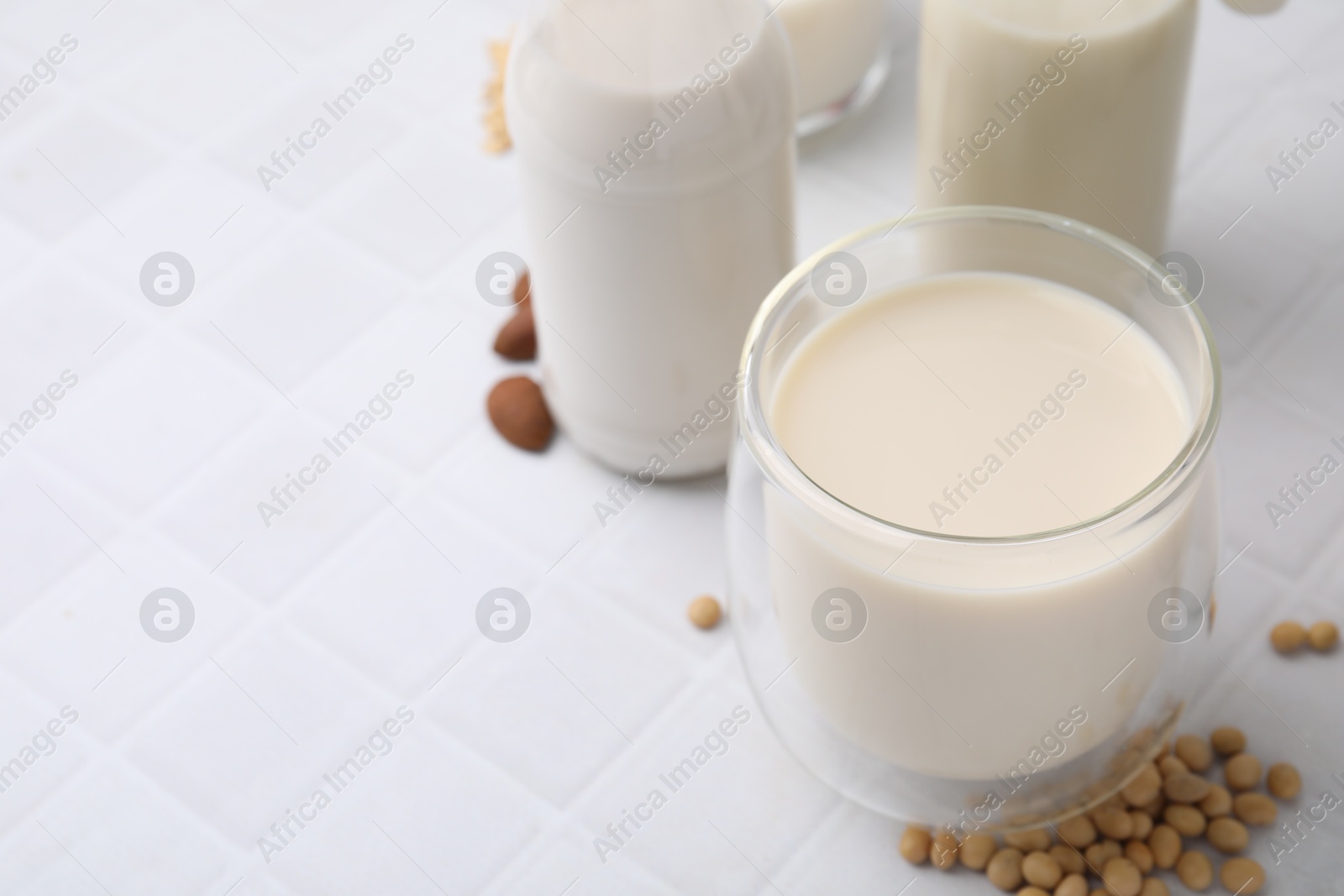 Photo of Different types of vegan milk and ingredients on white tiled table, closeup. Space for text