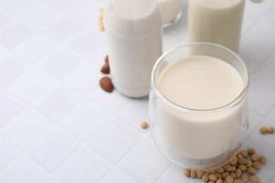 Photo of Different types of vegan milk and ingredients on white tiled table, closeup. Space for text